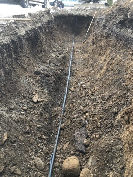 large excavation trench exposing underground residential water main for repair