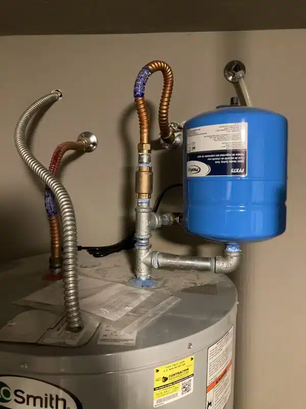 wider view of damaged water heater piping with visible corrosion and leak in residential home